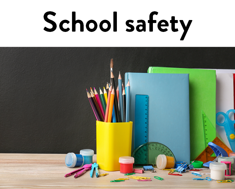 School safety. Brightly colored notebooks, pencils, paints and other school supplies on a desk with a chalkboard behind it.