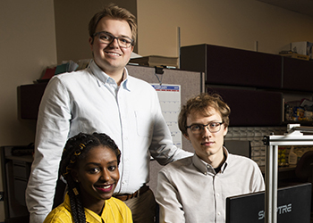three young adults, two seated, one standing, in front of a computer
