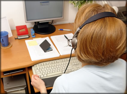 A woman wearing a headset working at a computer.