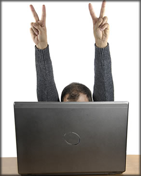 A man behind a laptop with both arms raised in the air.