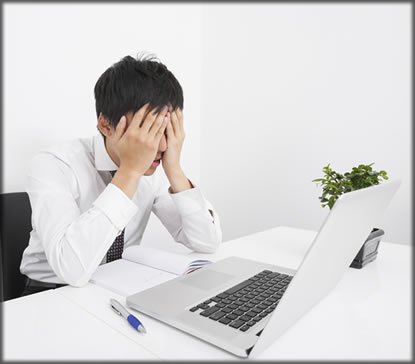 A frustrated man sitting at a laptop with his hands over his face.