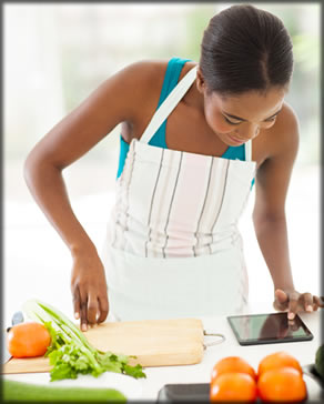 Woman cutting vegtables and reading a tablet.
