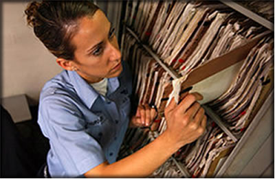 A woman searching through medical documents on a shelf.