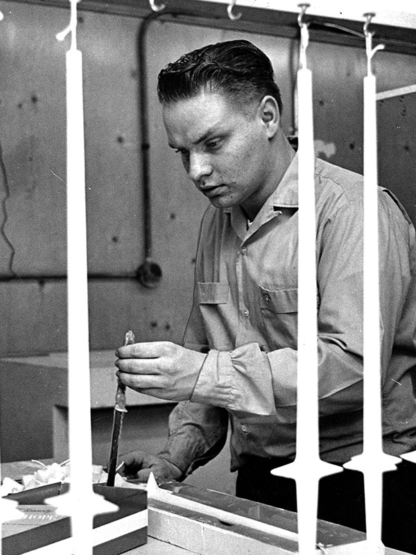 Photo of a young adult in work clothes using candle molds and dipping candles